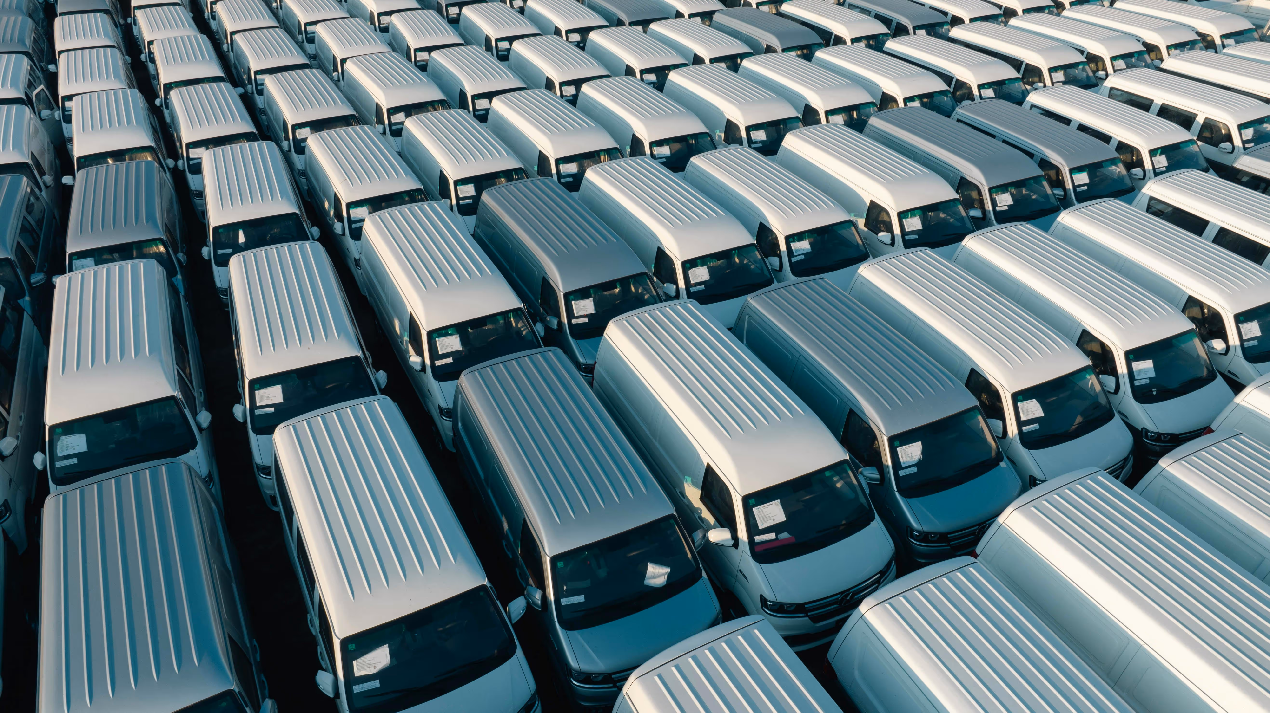 A fleet of white vans parked perfectly in multiple rows in a lot.