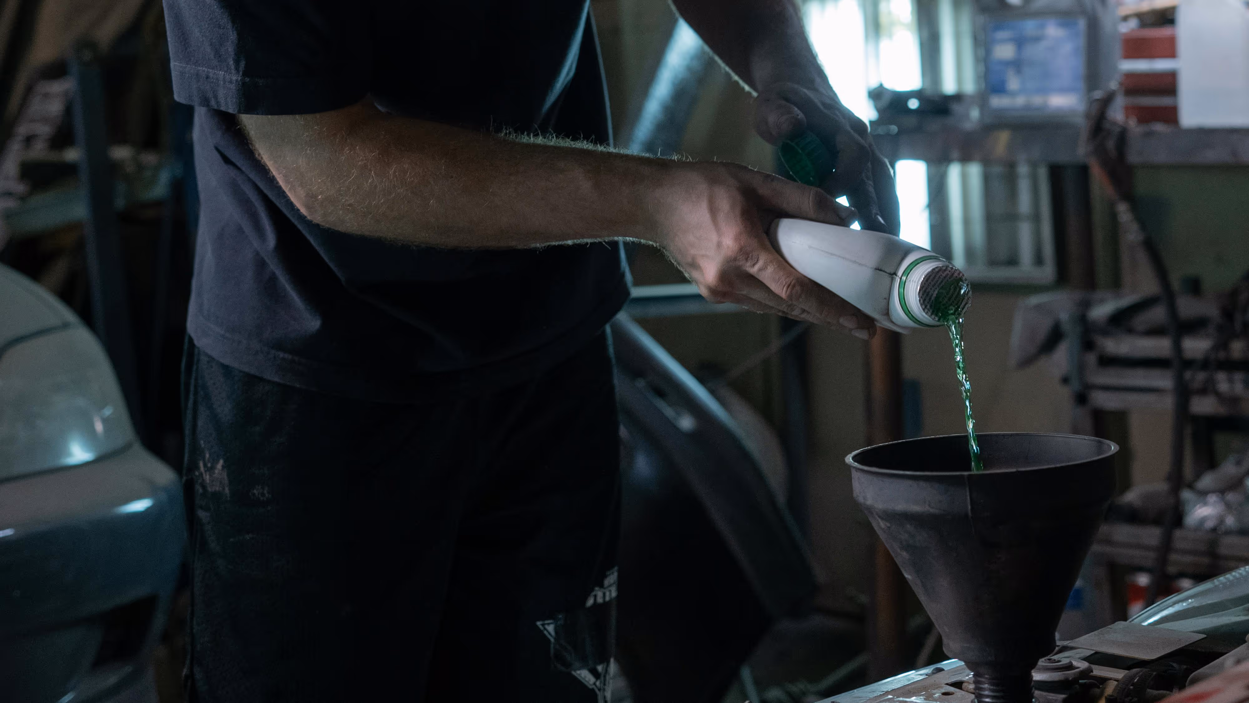 A mechanic holding a container and pouring a fluid through a funnel in a car compartment.
