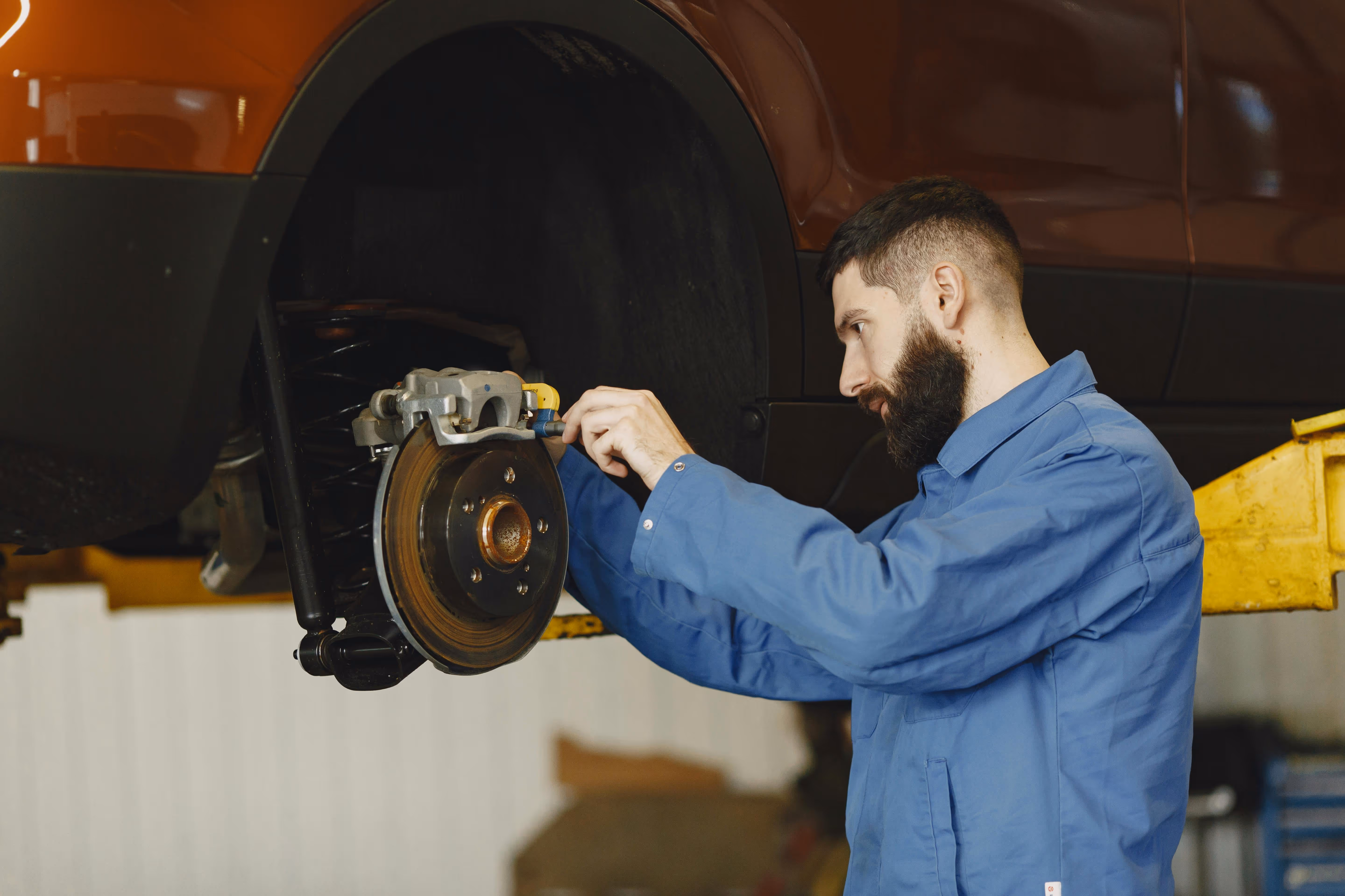 A mechanic examining a car's brake pads and rotors behind a removed whell.