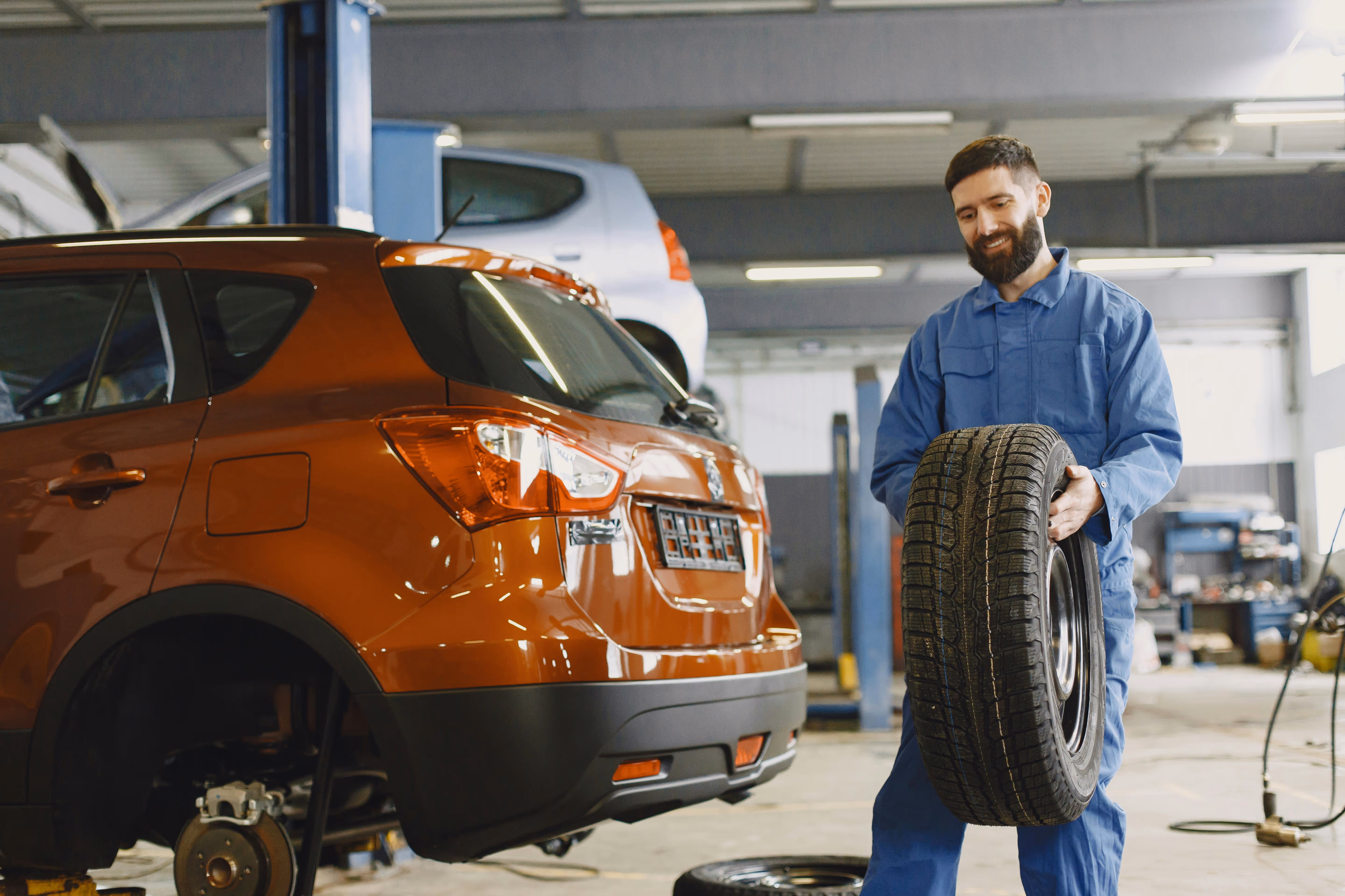 A mechanic smiling and carrying a wheel and tire for a red SUV car.