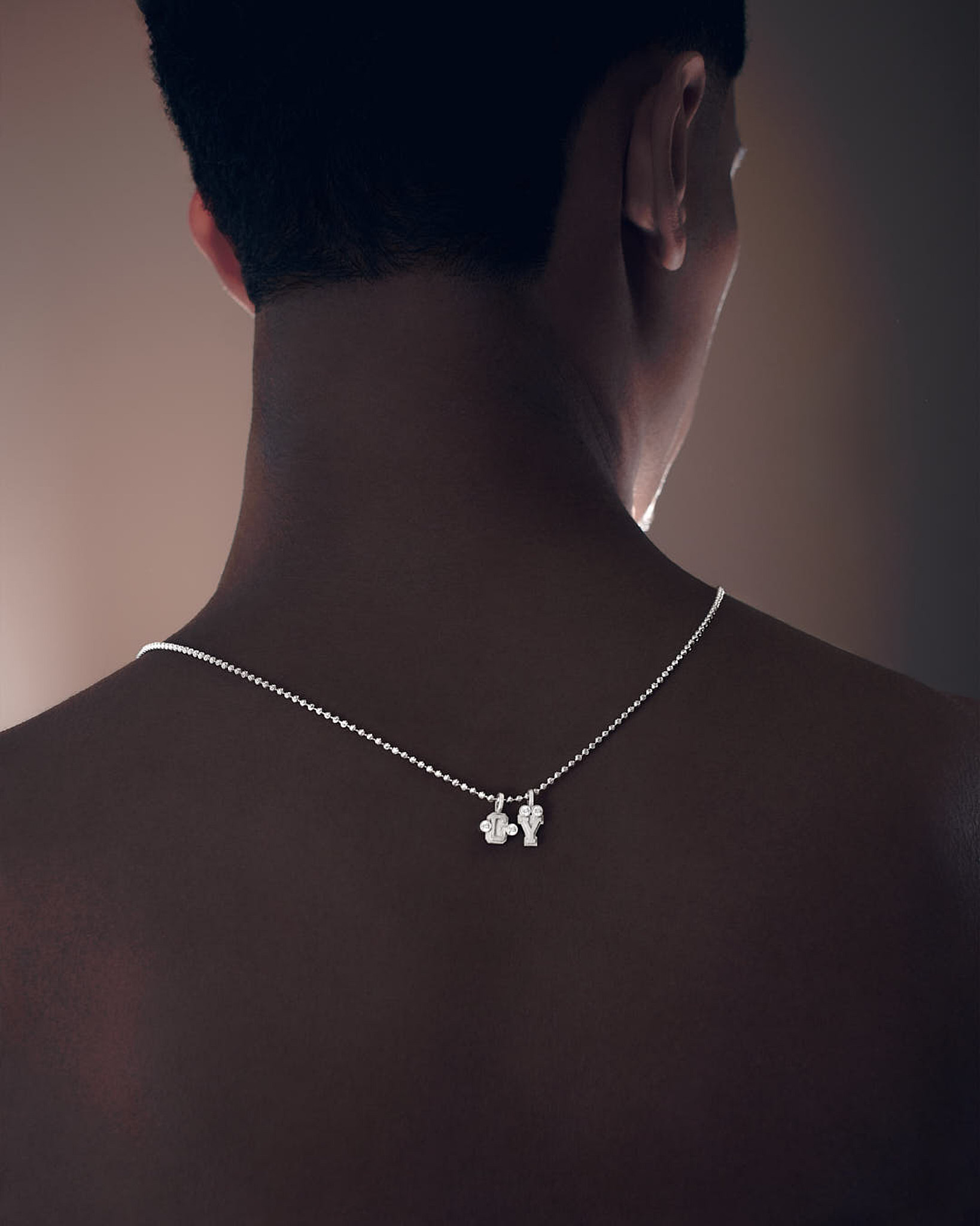 Close-up of a person's upper back and neck wearing a silver necklace with two small pendant charms.