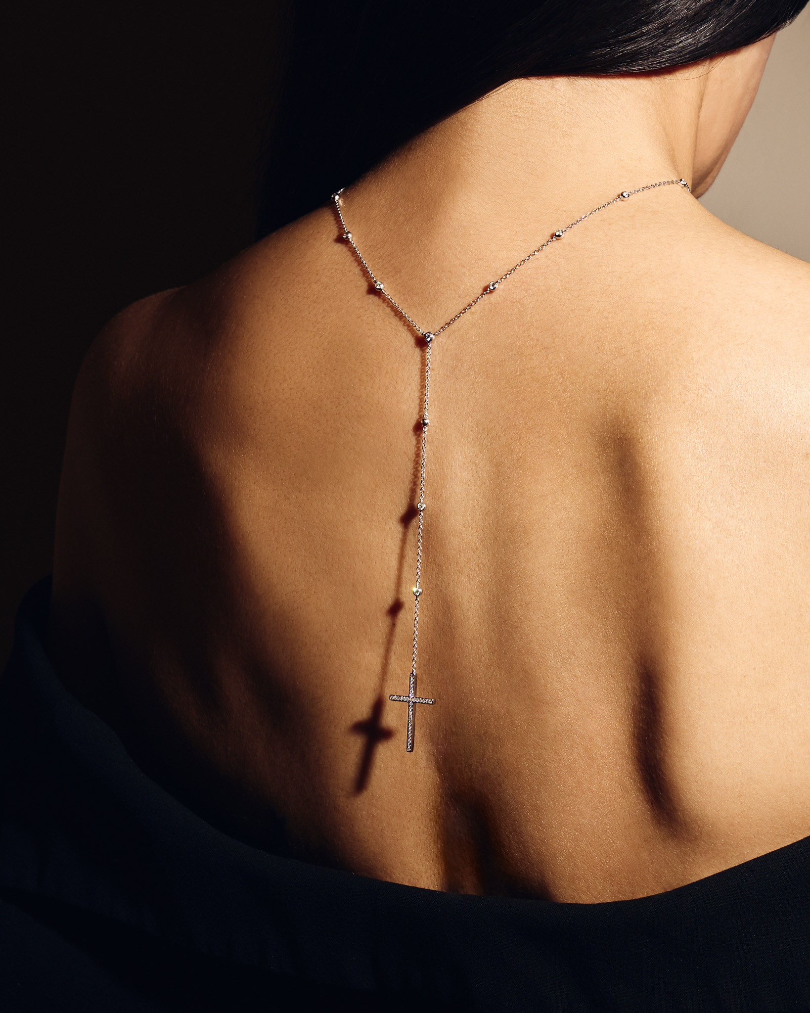 Back view of a person wearing a silver necklace with a cross pendant hanging down the spine.