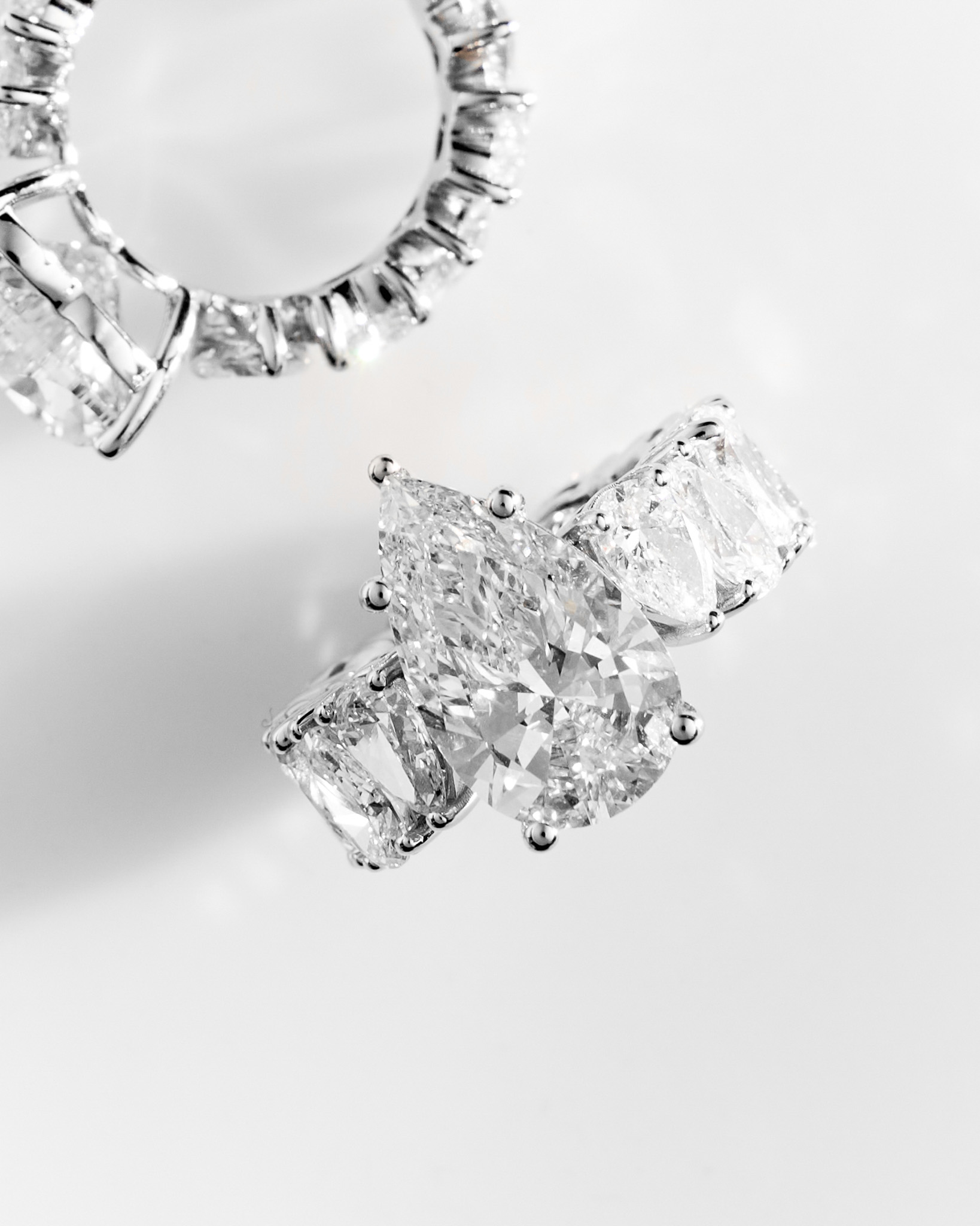 Close-up of a pear-shaped diamond ring with additional large diamonds set on the band, displayed on a white background.
