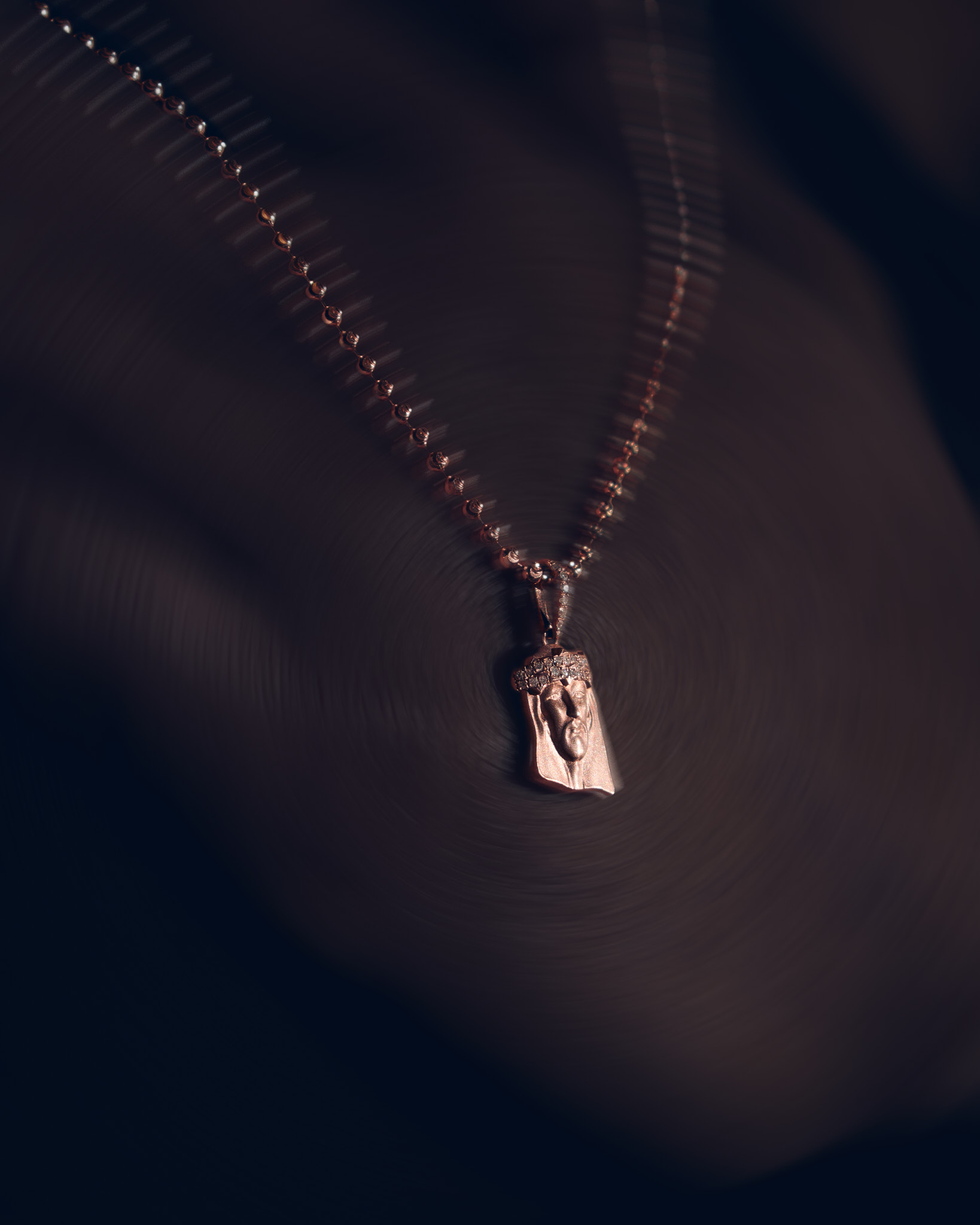 Close-up of a gold pendant with a carved face wearing a jeweled crown on a gold beaded chain.