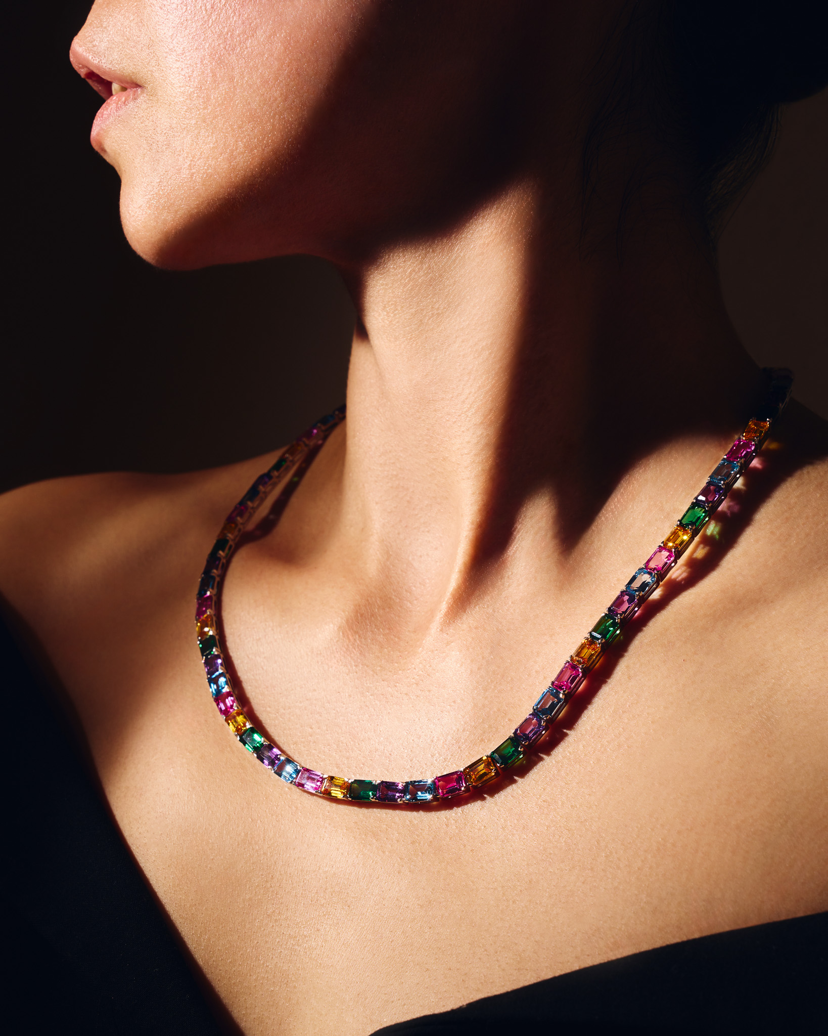 Close-up of a woman's neck and shoulders wearing a multicolored gemstone necklace.