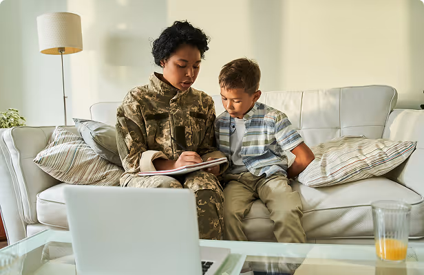 A warm, candid image of a parent and a child sitting together on a couch, looking at and using a laptop computer.