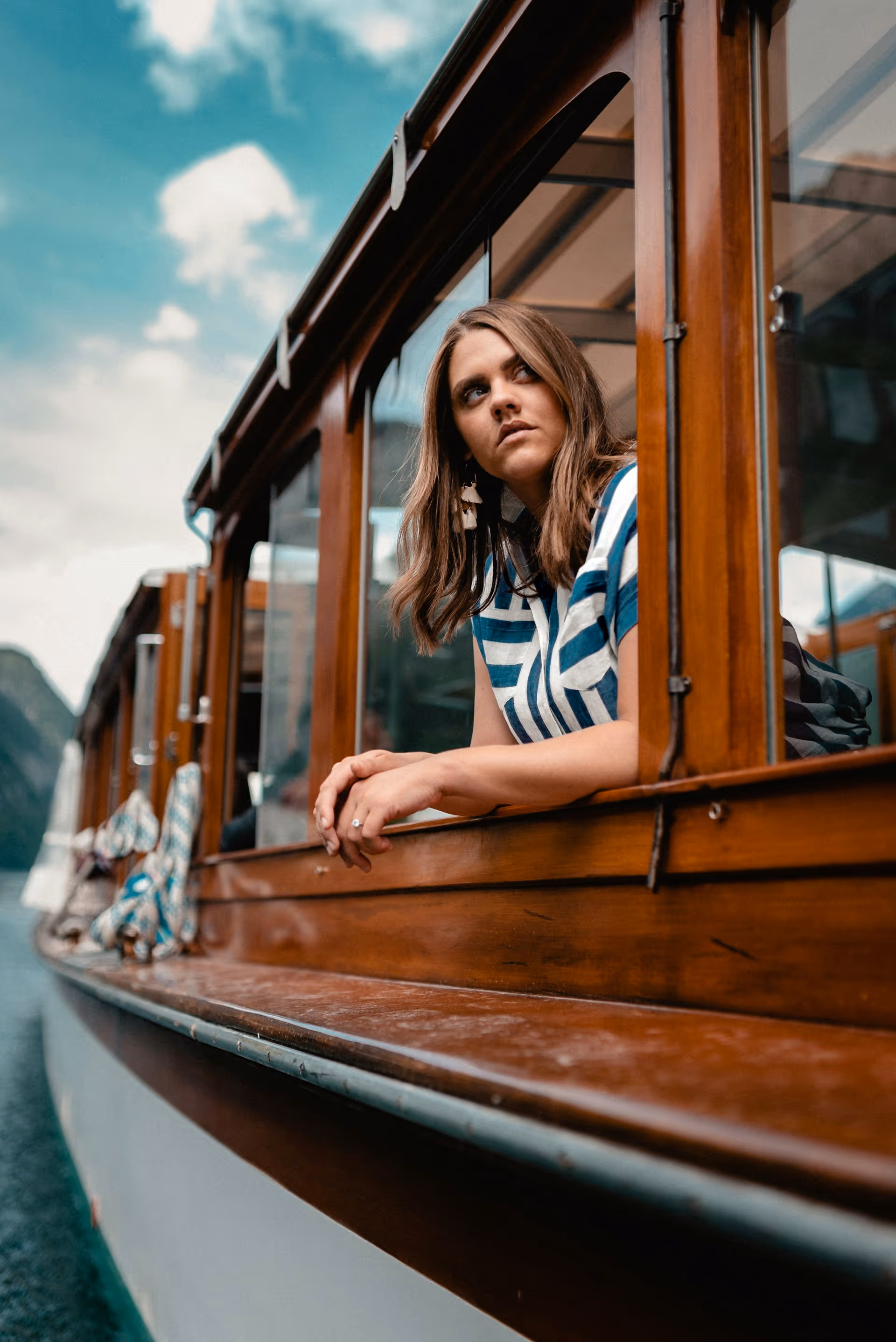 A close-up shot of a young woman with long hair looking out the open window of a vintage-style streetcar or trolley.
