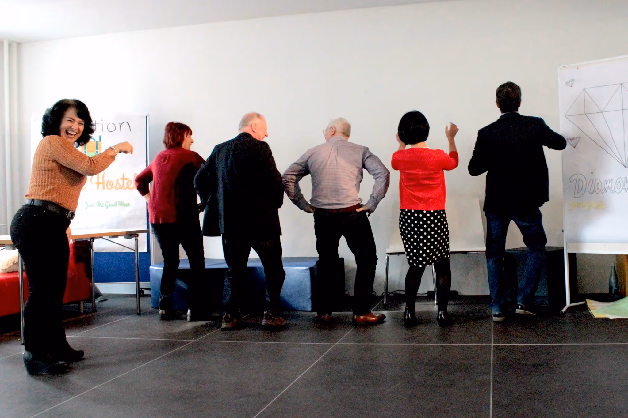 A diverse group of people (students or children) are standing in a semicircle facing the camera, possibly warming up or engaging in a group activity.