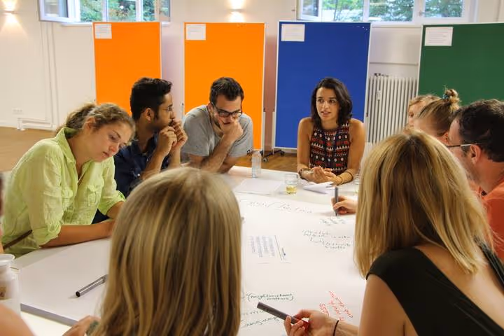 A group of people sitting around a bright table, engaged in a discussion or brainstorming session in an office environment.