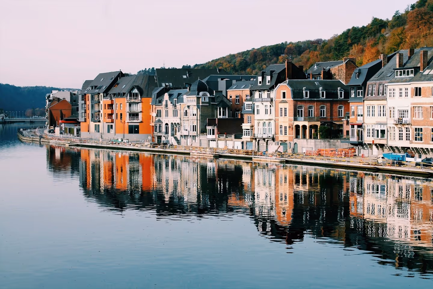 A picturesque view of quaint houses reflected in the still water of a lake or canal, surrounded by trees.