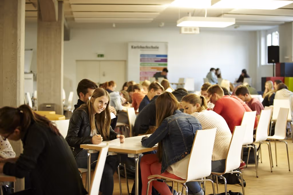 A medium shot of a large group of people seated at tables, facing a presentation screen or speaker during an academic event.