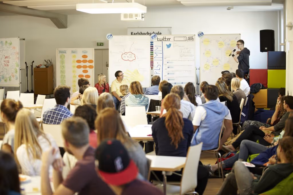 A brightly lit seminar or classroom with many attendees seated at tables, actively engaged in a group discussion or workshop.