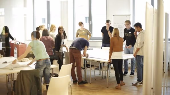 A wide shot of a classroom or seminar with a group of students and faculty seated at tables, engaged in a discussion or lecture.