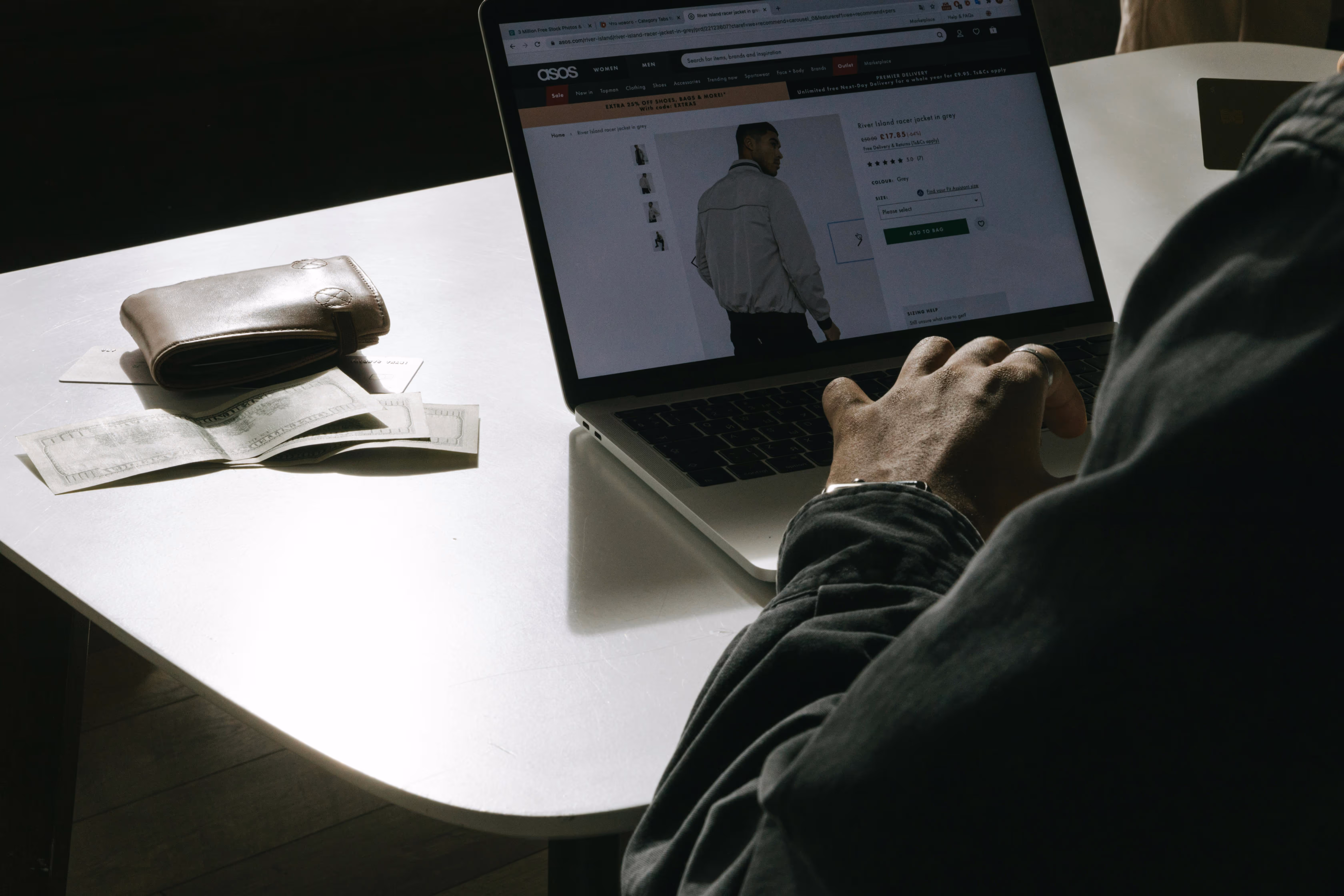 Ecommerce owner working on his store on a laptop on a desk next to some cash