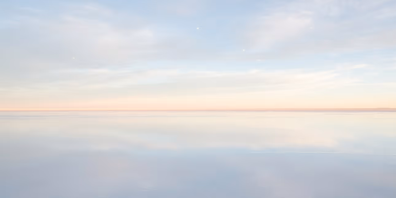 Ciel lumineux avec des nuages légers se reflétant sur une surface d'eau calme au coucher du soleil.
