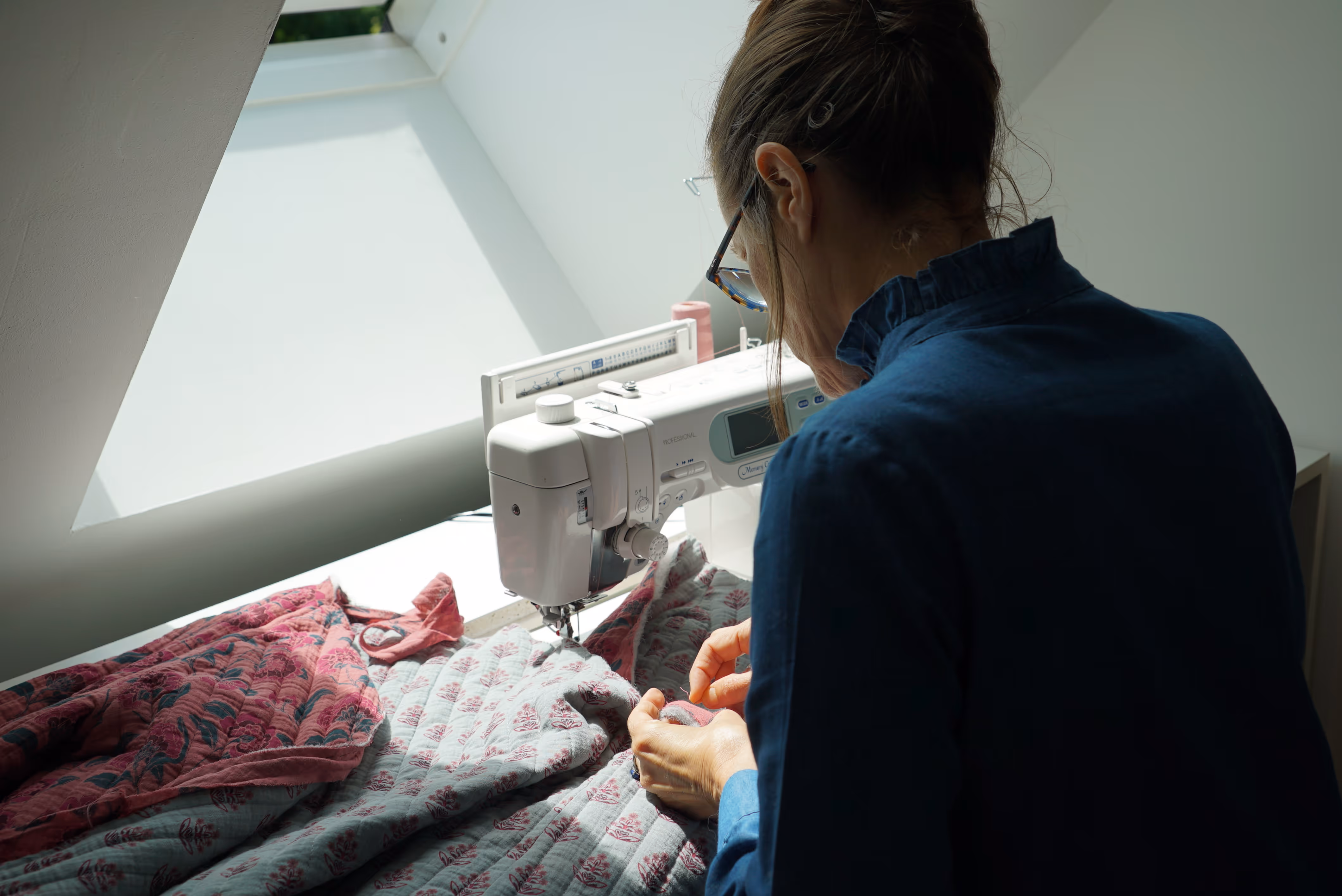Des femmes travaillent ensemble dans un atelier de couture, découpant et assemblant des tissus sur des tables bien éclairées.