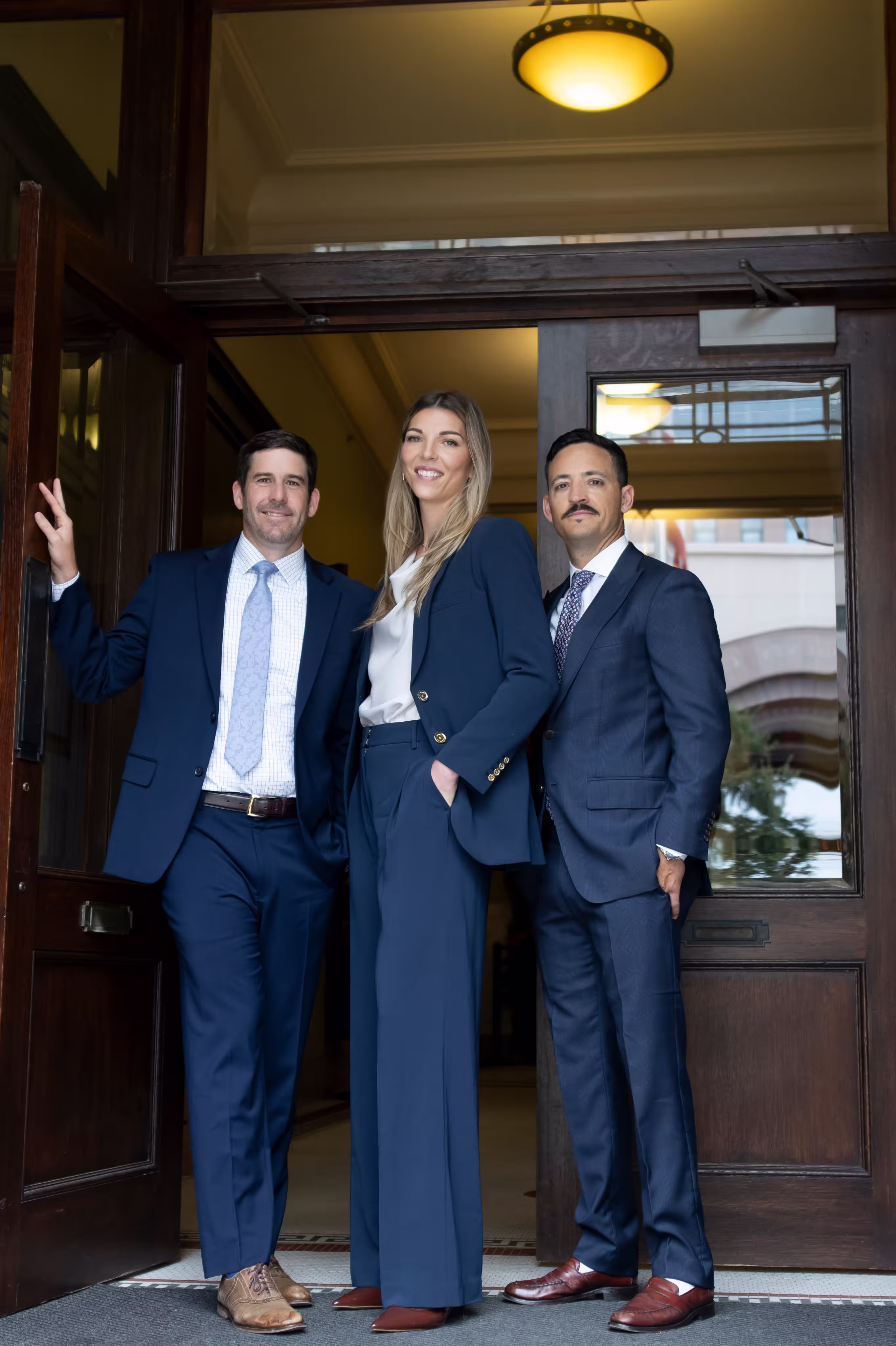 Three people in business attire standing by a wooden door entrance.