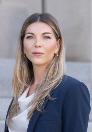 Woman with long light brown hair wearing a white blouse and navy blazer.
