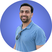 Smiling man with short dark hair and beard wearing a blue polo shirt and sunglasses on collar.