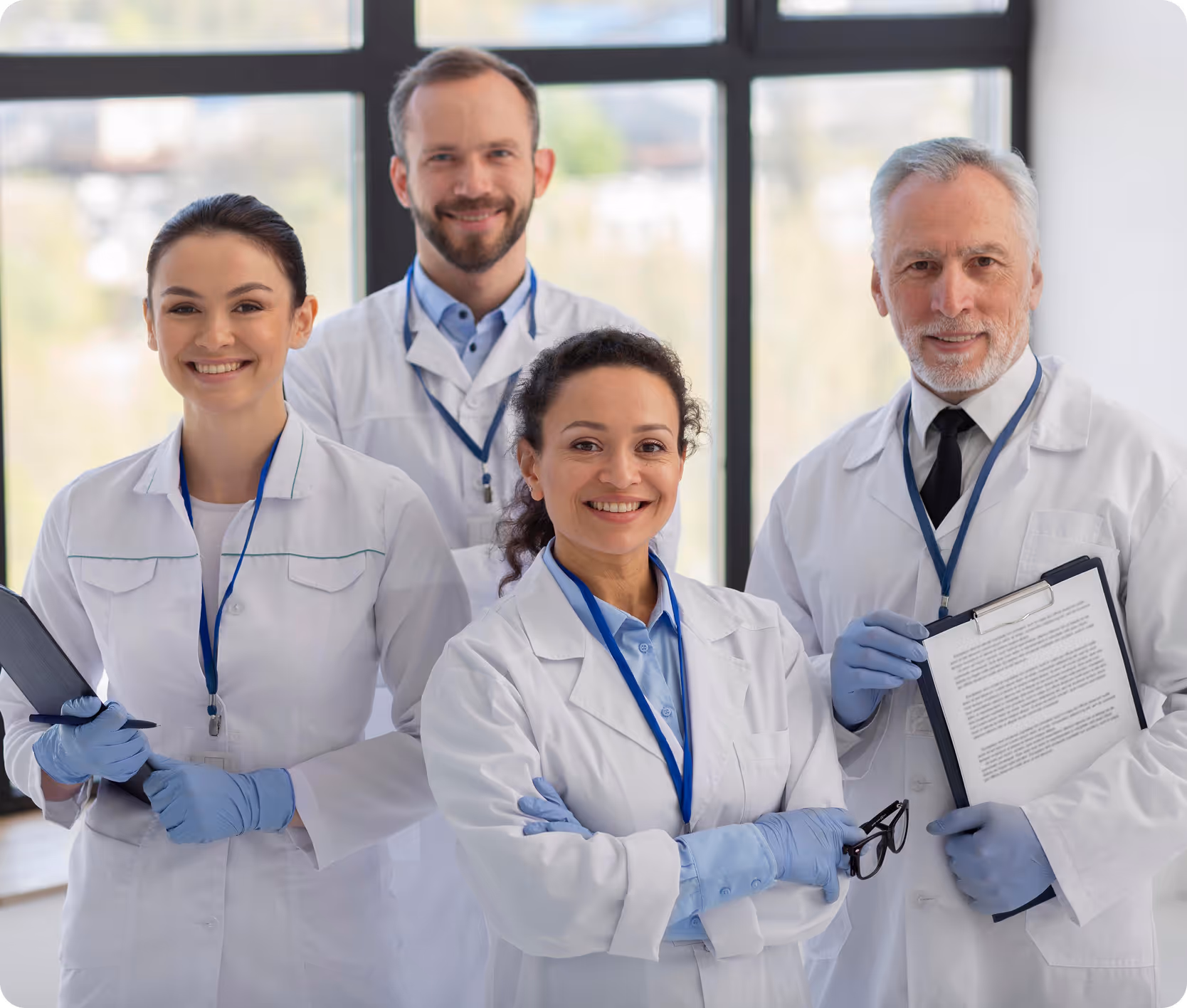 Four physicians in white coats wearing ID badges, holding clipboards and smiling