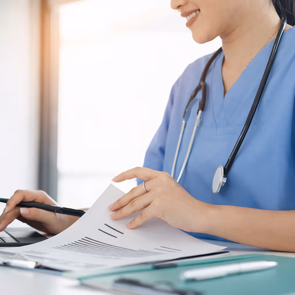 Female doctor in blue scrubs reviewing a chart with a laptop open on her desk