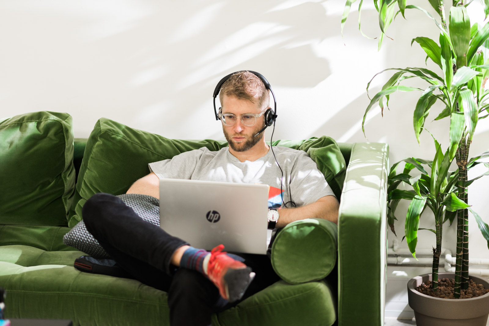 A person wearing headphones is sitting on a green couch, using a laptop.