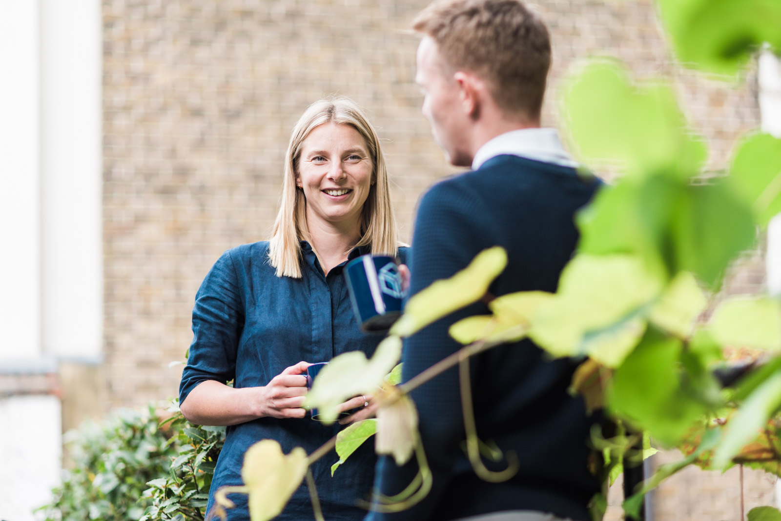 Two people having a conversation outdoors, with green leaves in the foreground.