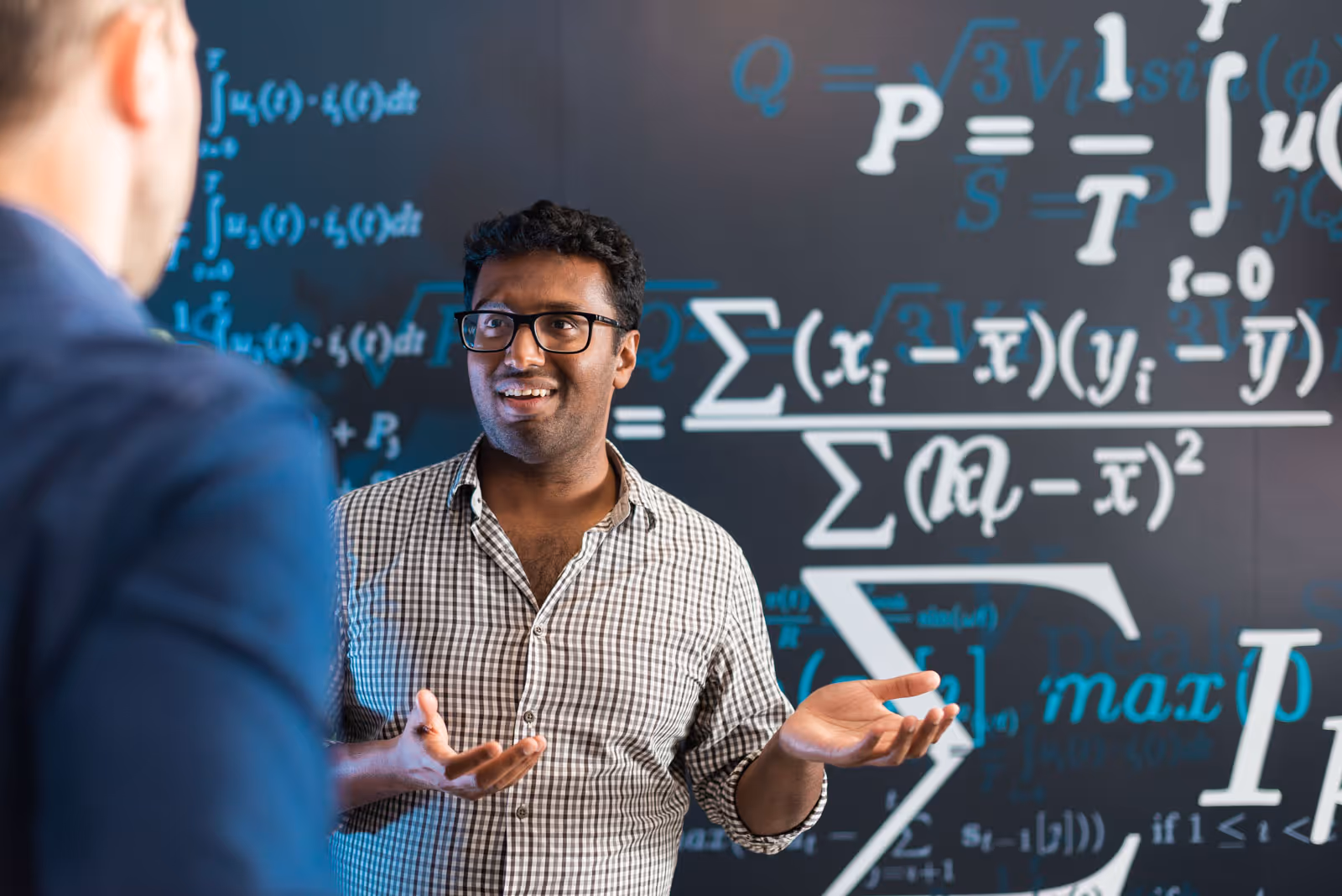 Person gesturing while talking in front of a chalkboard with mathematical equations.