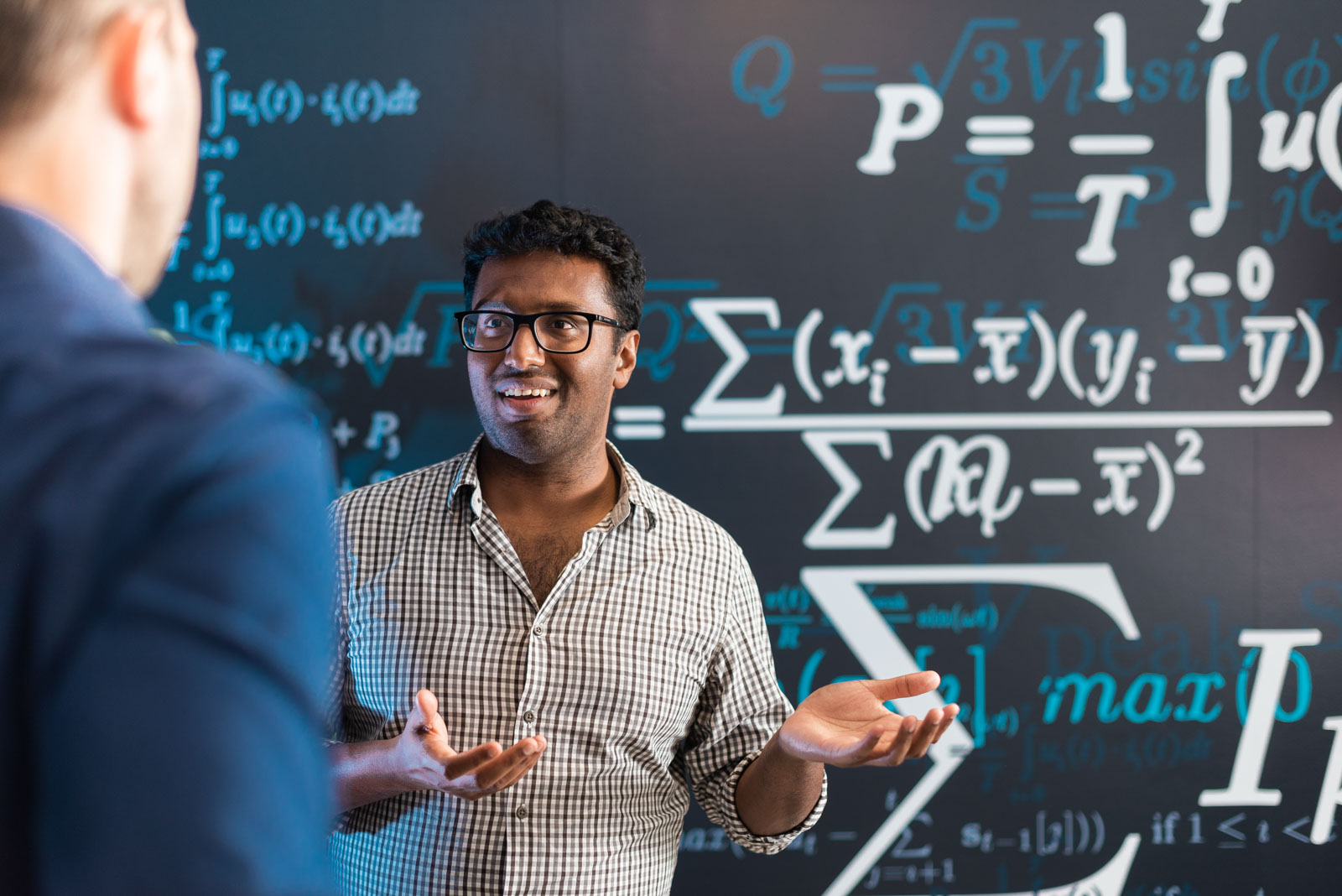 Person gesturing while talking in front of a chalkboard with mathematical equations.