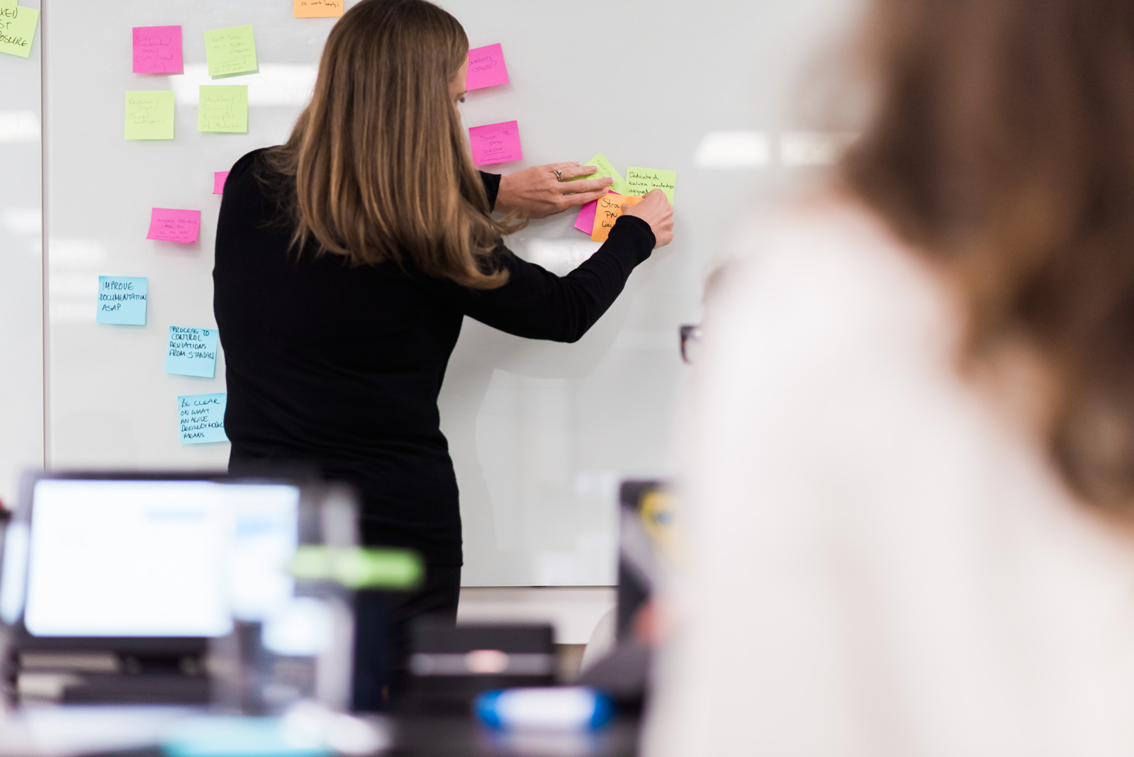 A woman places sticky notes on a whiteboard in an office setting.