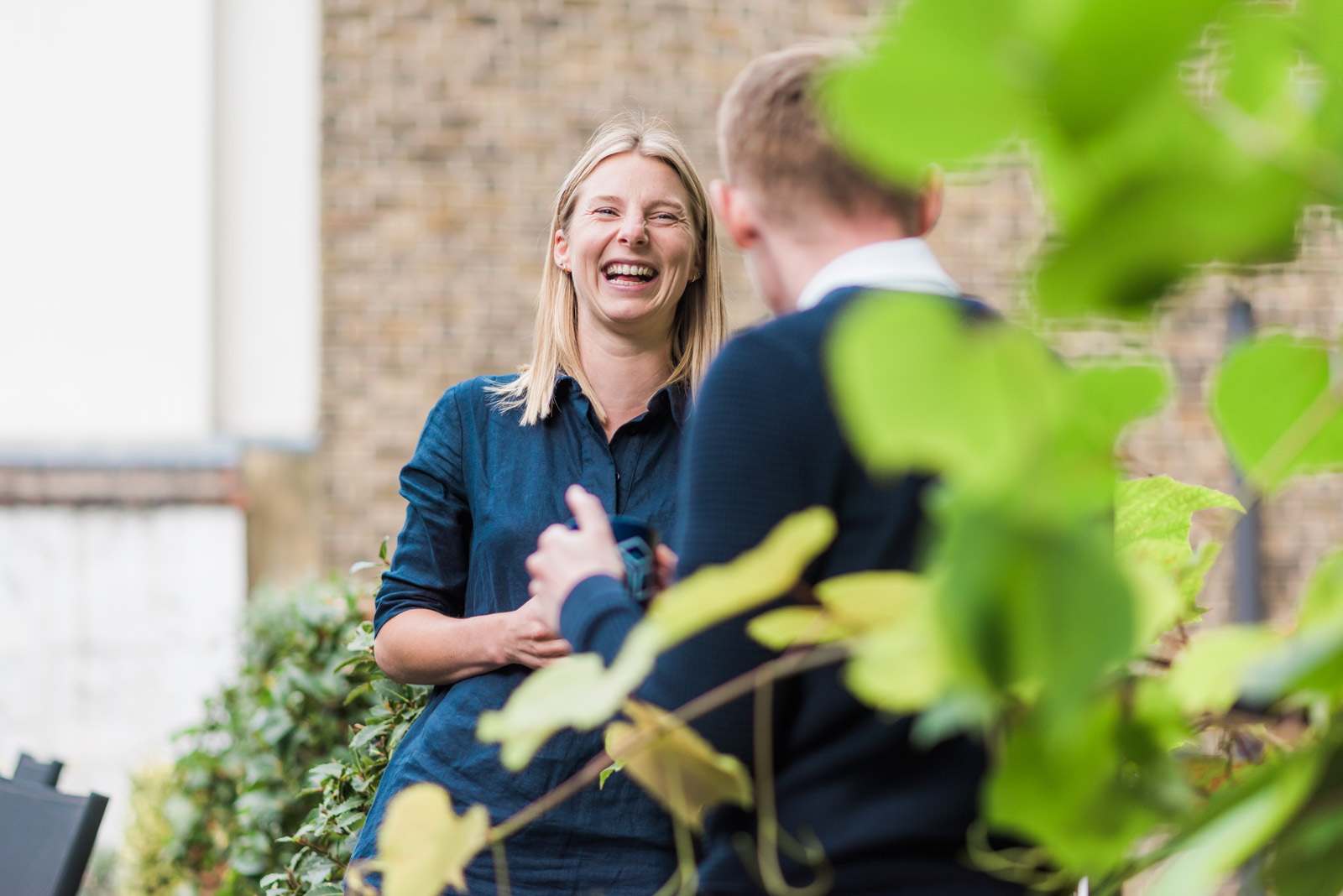 A woman in a blue shirt laughs while talking to a man outdoors.