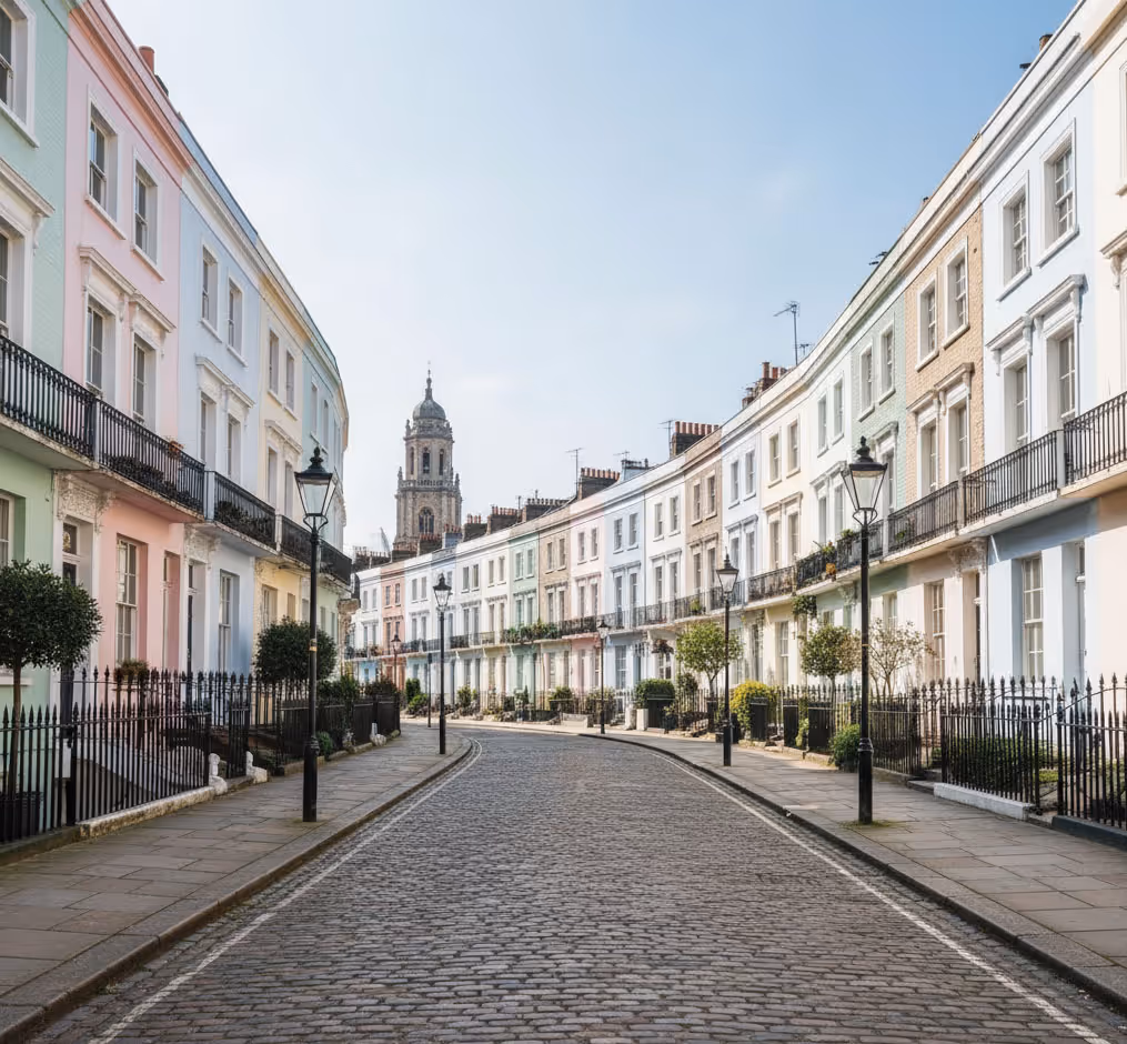 A quiet, curved street with pastel-colored houses and a tower visible in the background.
