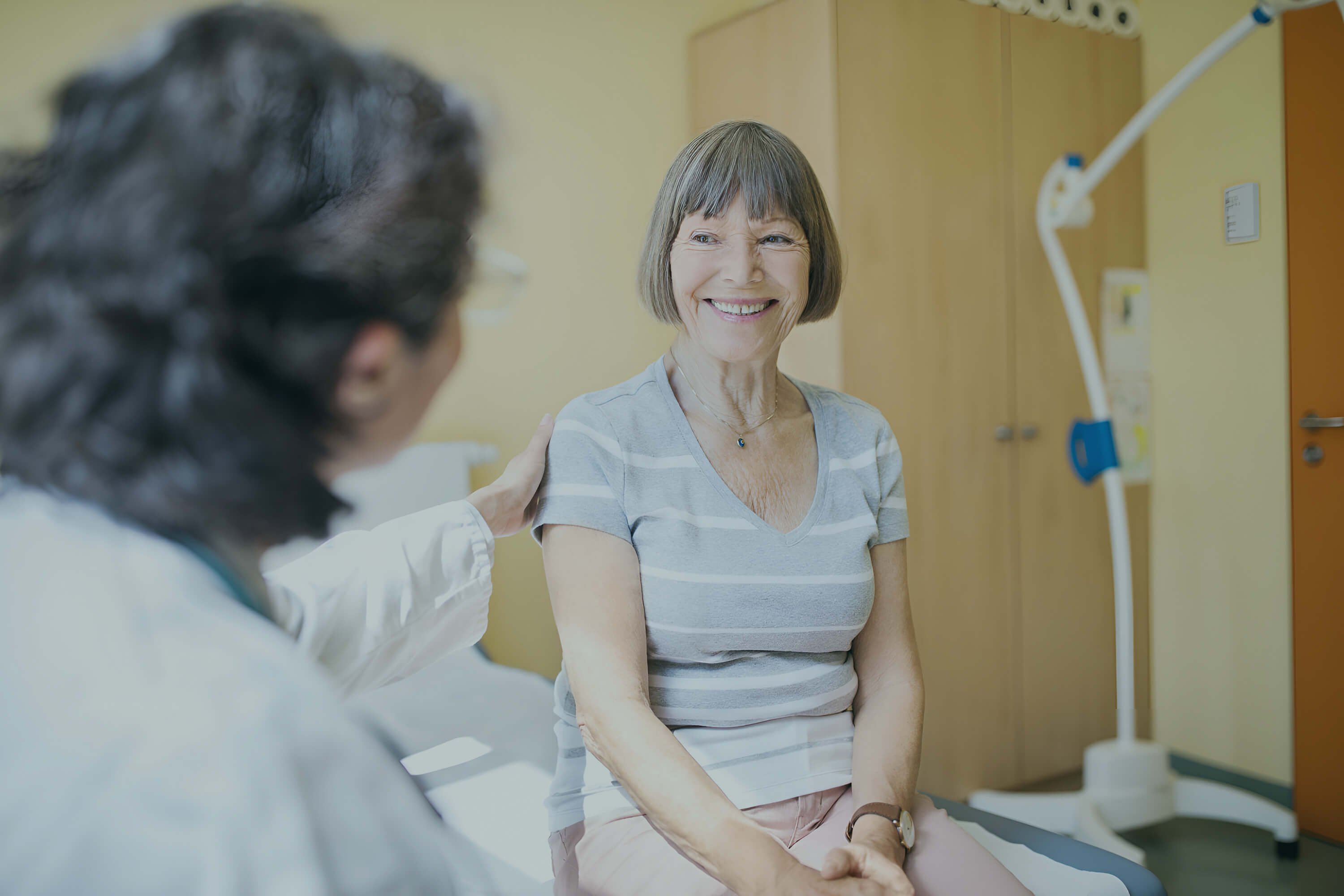 Oudere patiënte glimlacht gerustgesteld tijdens gesprek met een arts in een radiologiepraktijk