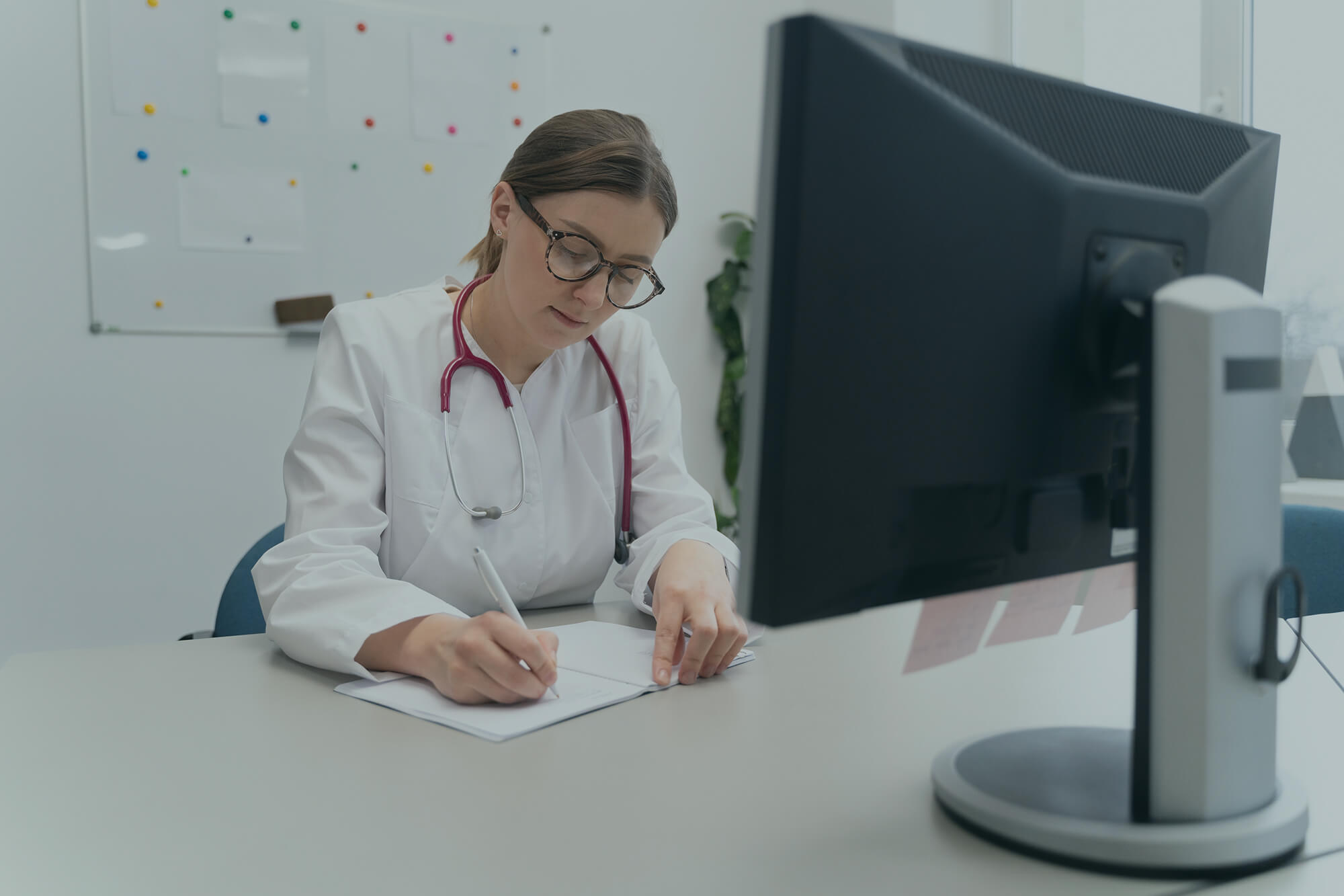 Huisarts schrijft een medische aanvraag op papier terwijl zij aan haar bureau werkt, ter illustratie van een patiëntdoorverwijzing.