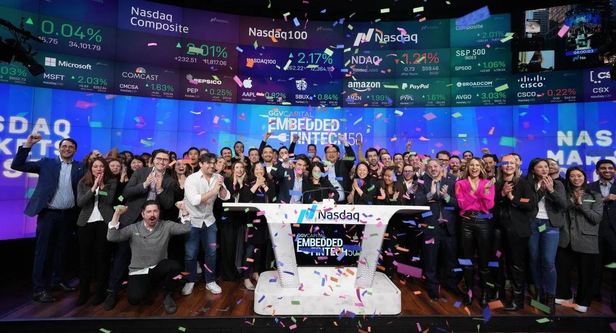 Group of people celebrating with confetti in front of Nasdaq stock market screens during Embedded Fintech 150 event.