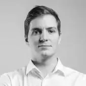 Portrait of a young man with short hair wearing a white collared shirt against a plain gray background.