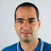 Headshot of a man with short dark hair, wearing a blue collared shirt, smiling slightly against a plain light background.