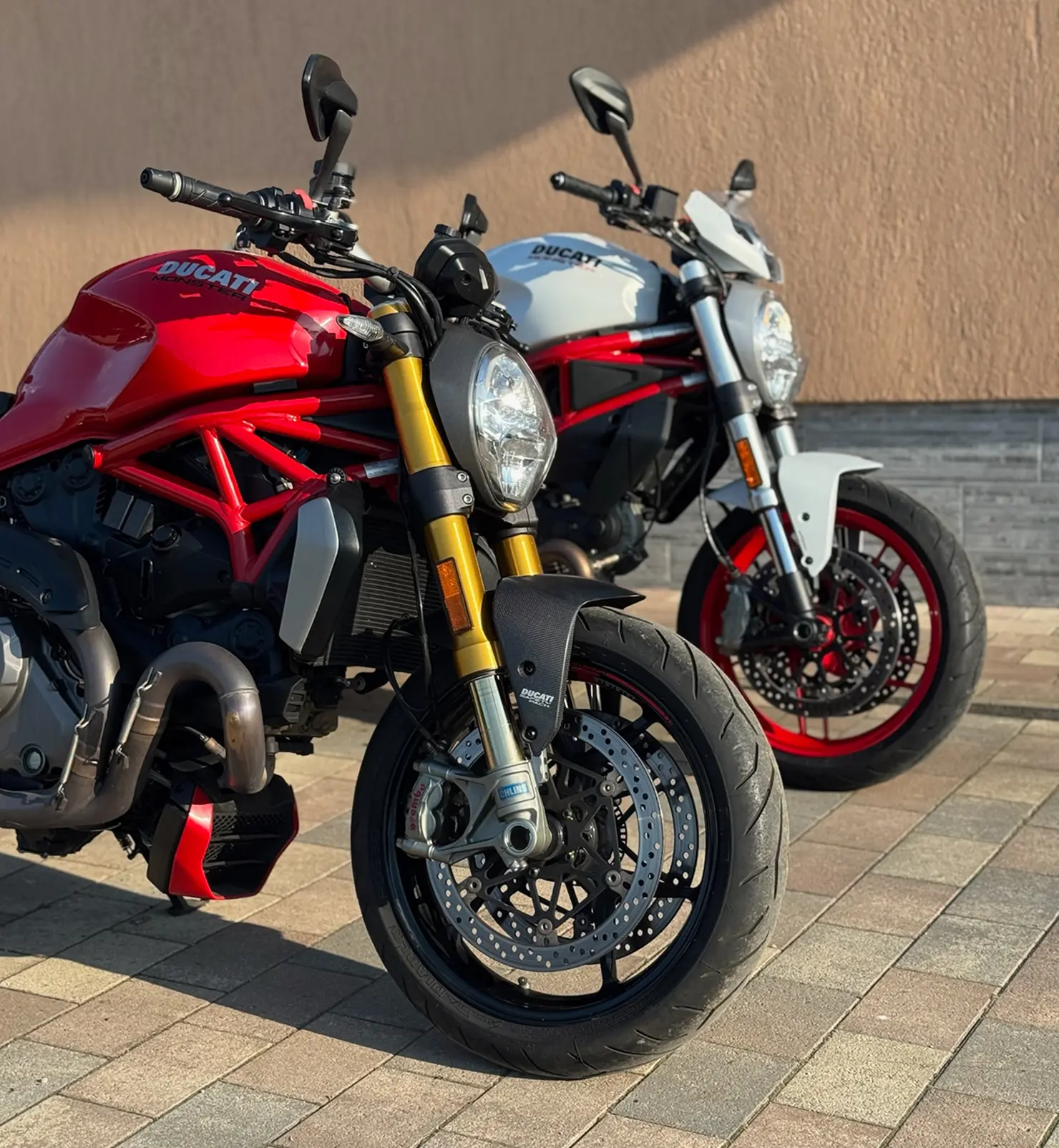 Egy piros és egy fehér motor egy térkövezett udvaron házhozszállítás után.