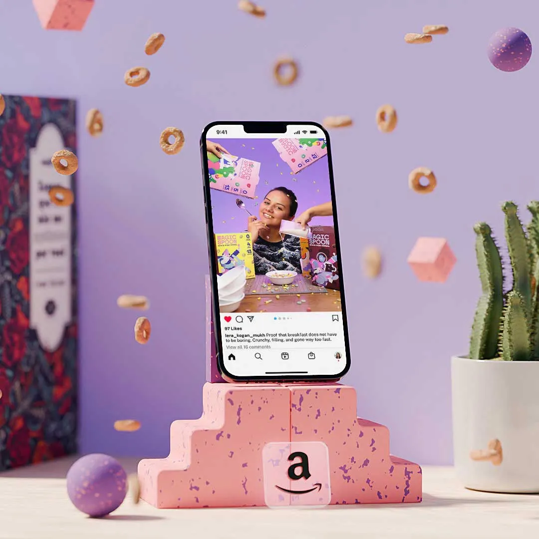 Smartphone on a pink speckled stand showing Instagram post of a woman with cereal boxes, with cereal pieces floating around and a cactus in a white pot on the side.