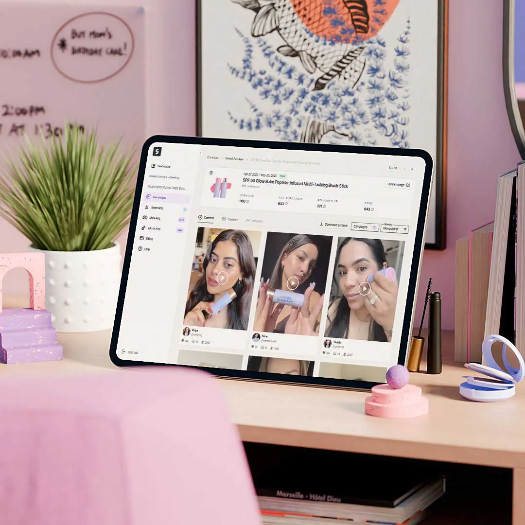 Tablet displaying a social media dashboard with beauty product videos, placed on a desk with makeup items and a potted plant.