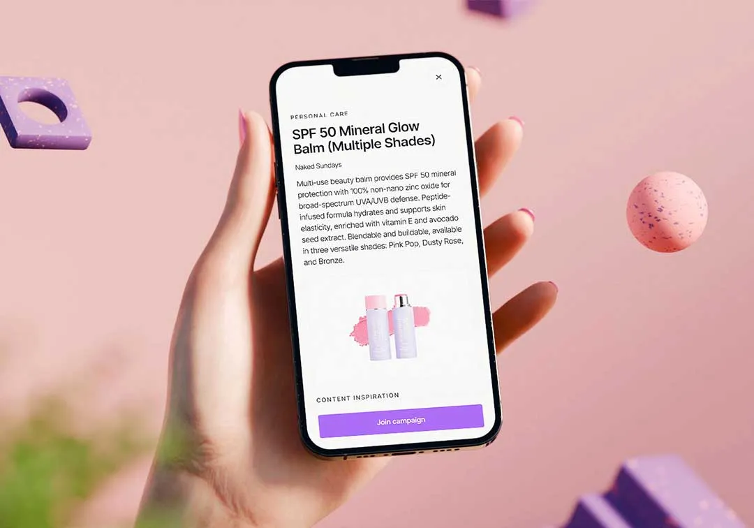 Hand holding a smartphone displaying product details with image of two balm bottles on a pink background.