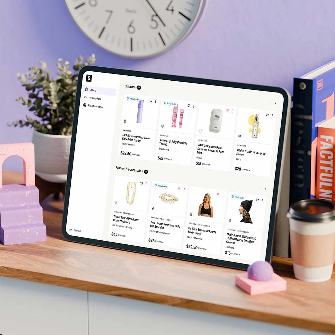 Tablet on wooden desk displaying an online shopping page with skincare and fashion accessories, surrounded by a potted plant, clock, books, and a takeaway coffee cup.