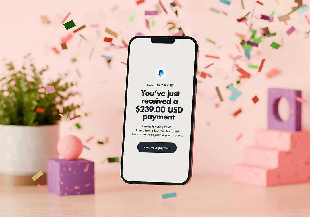 Smartphone displaying a PayPal notification for a payment received, with colorful confetti falling.