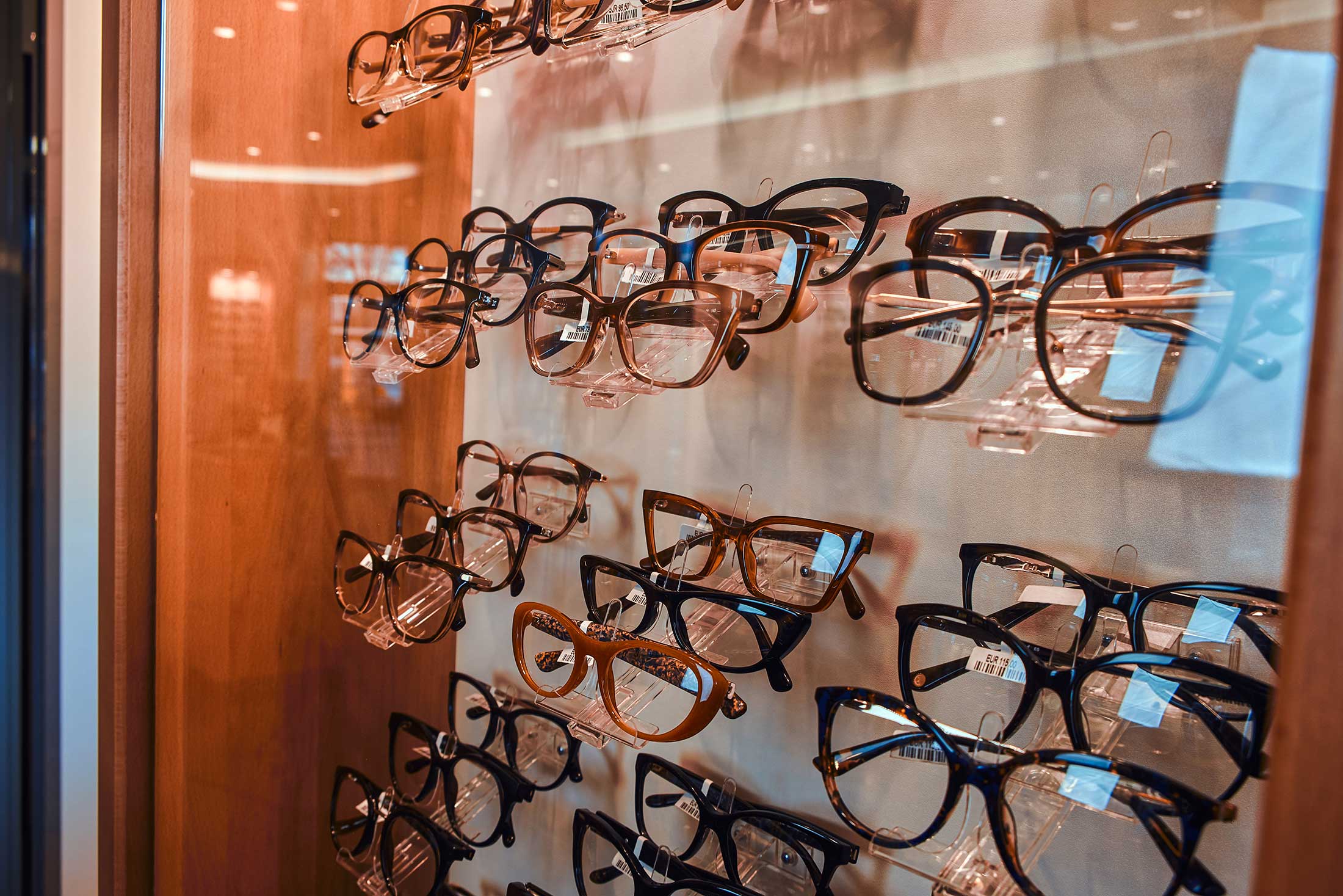 Multiple eyeglasses displayed on clear stands in an optical store window