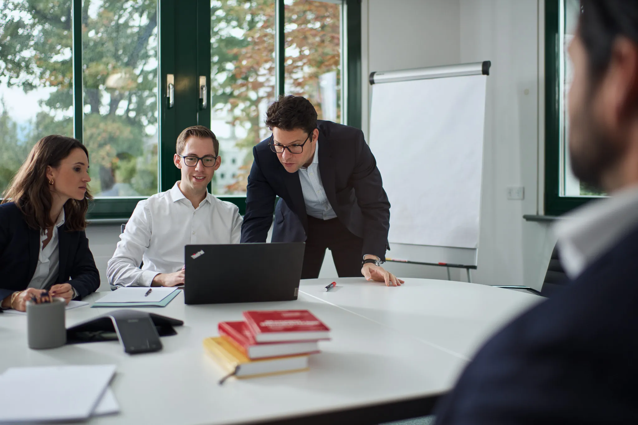 Vier Personen in einem Büromeeting schauen gemeinsam auf einen Laptop vor einem Flipchart.