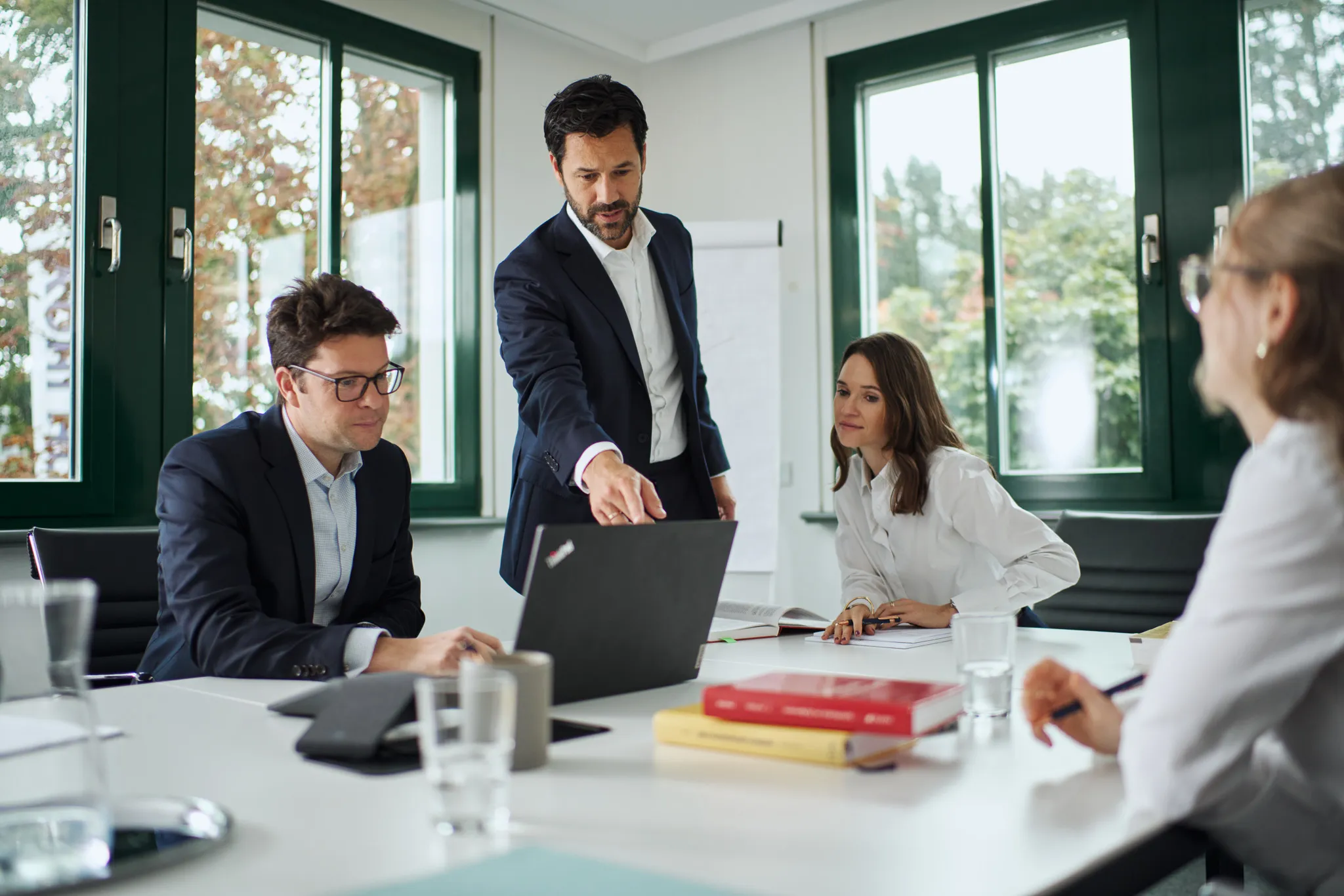 Vier Geschäftsleute diskutieren in einem hellen Büro um einen Tisch, wobei ein Mann auf den Bildschirm eines Laptops zeigt.
