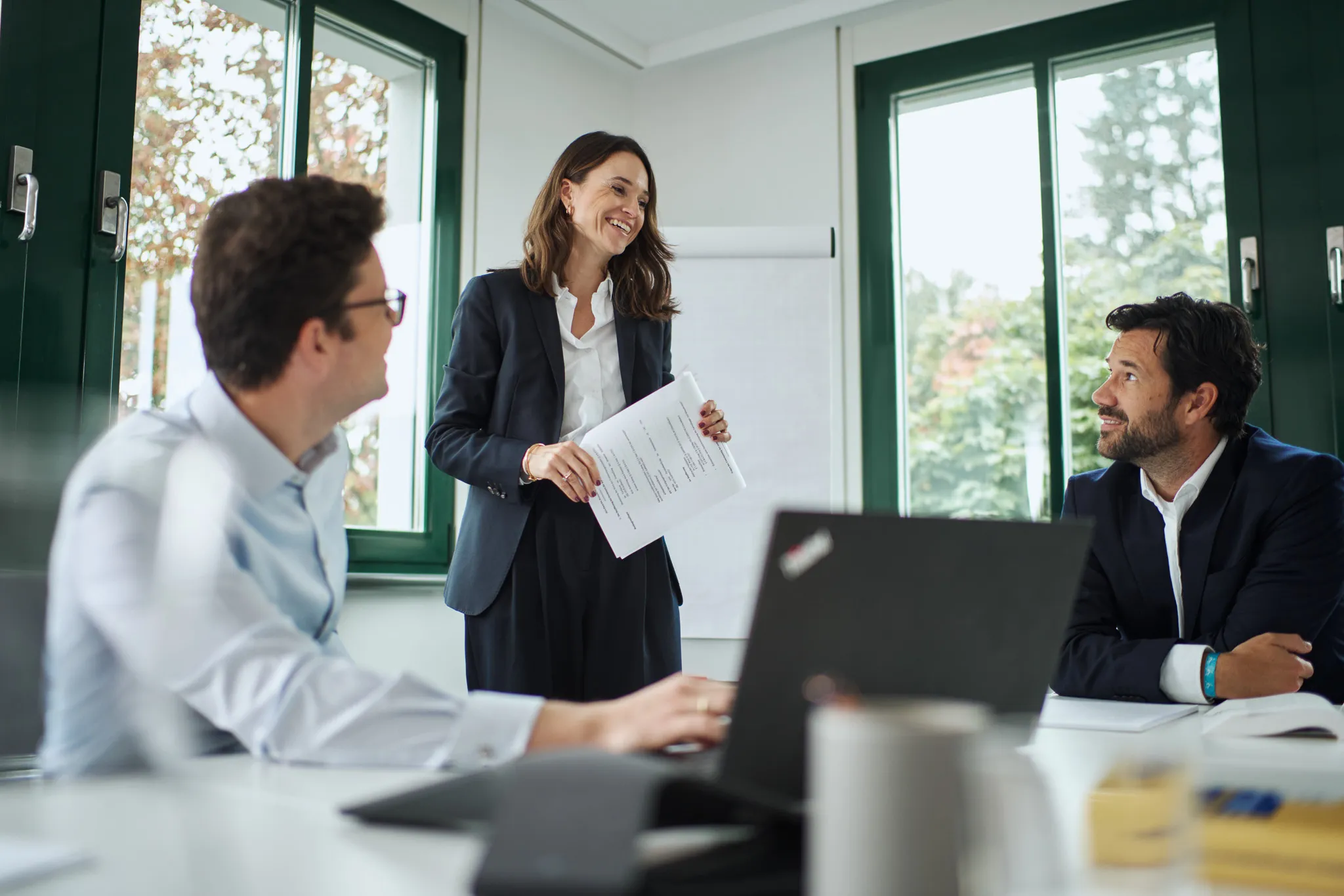 Drei Geschäftspersonen in einem hellen Büro besprechen dokumente während eines Meetings.