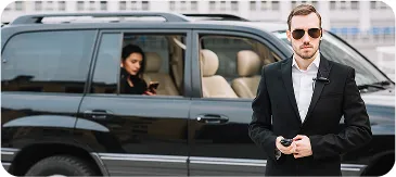 Professional chauffeur standing beside a luxury black SUV while a passenger waits inside, representing high-end private taxi or executive transport service