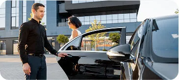 Luxury car service in Denver with professional chauffeur opening door for businesswoman outside modern office building
