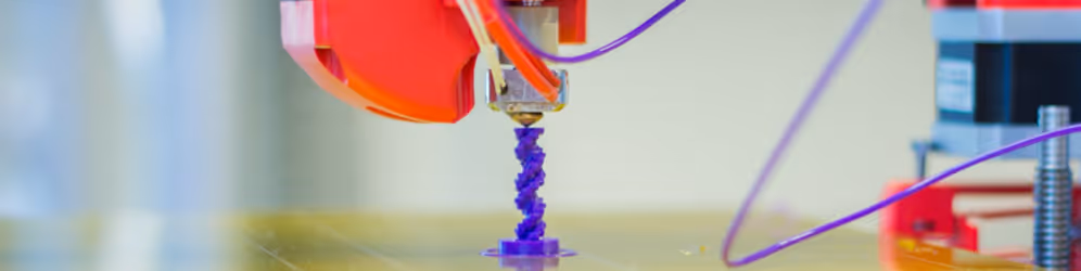 A young woman working in a machine shop. She is looking directly towards the camera, and is surrounded by men.
